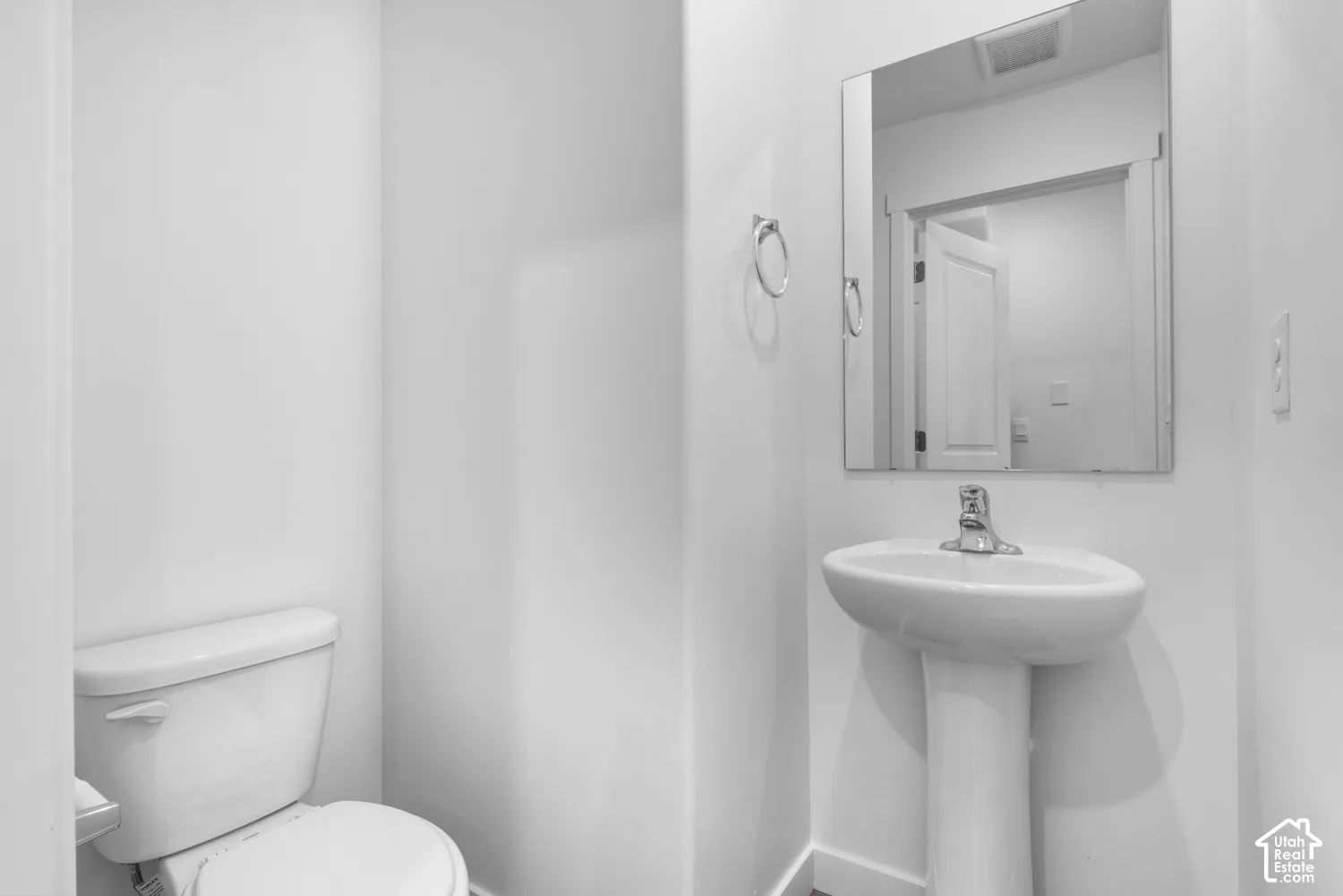 Pedestal sink with chrome faucet, wall-mounted mirror, and white toilet