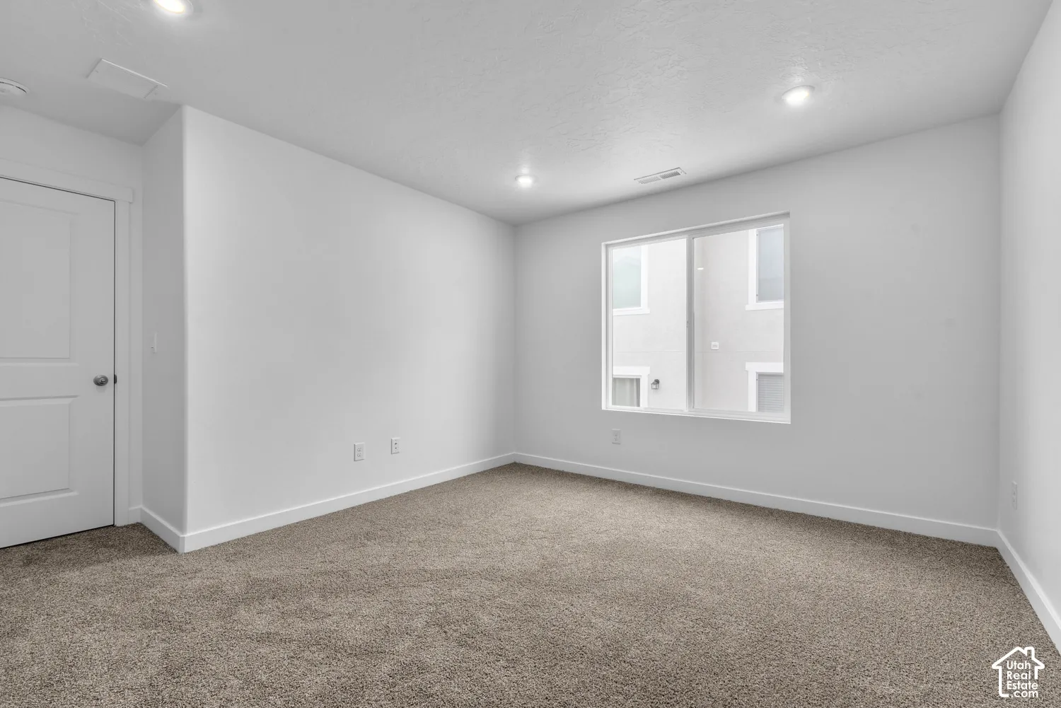 Recessed ceiling lighting, white interior door, light-colored carpeting, white wall finishes, and a framed window
