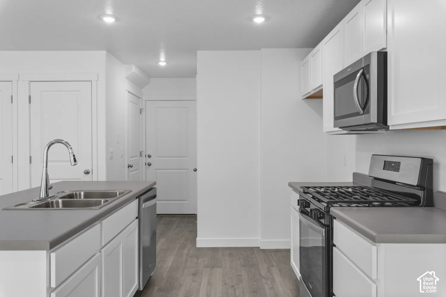 Kitchen featuring white cabinetry, grey countertops, stainless steel appliances, and wood-finish flooring