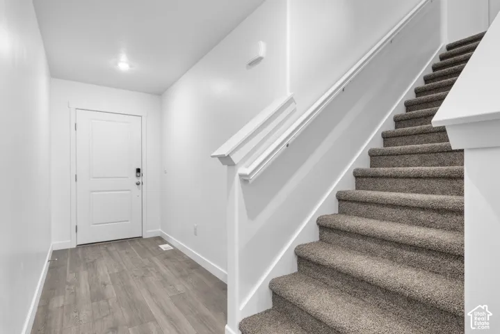 Entryway featuring wood-finish flooring, a contemporary white door, and a staircase with plush carpeting and a white handrail