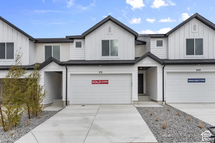 Modern townhouse exterior featuring white vertical siding, black trim, and a concrete driveway