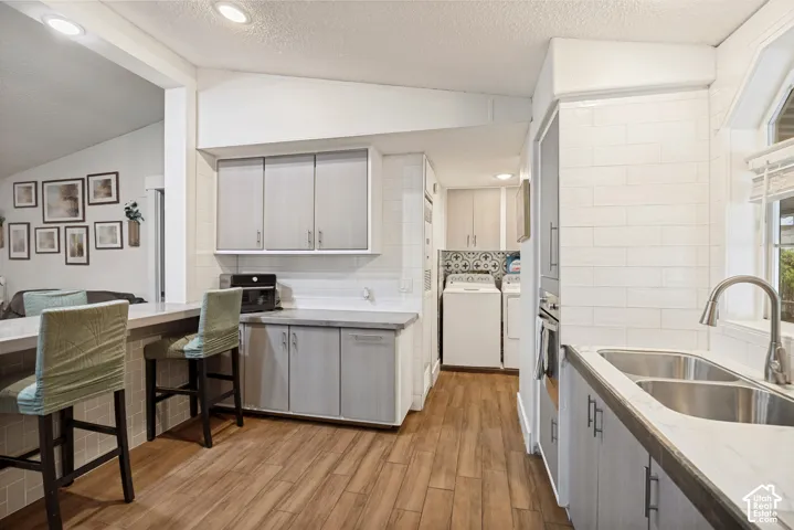 Kitchen featuring wood-finish flooring, light grey cabinetry, built-in dual basin sink, and white subway tile backsplash