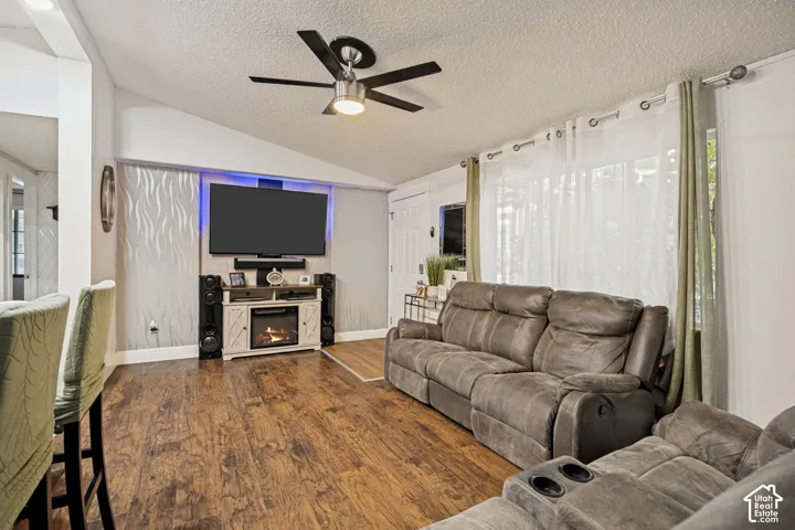 Vaulted ceiling with a ceiling fan, wood-finish flooring, built-in media console with integrated fireplace, and a large window