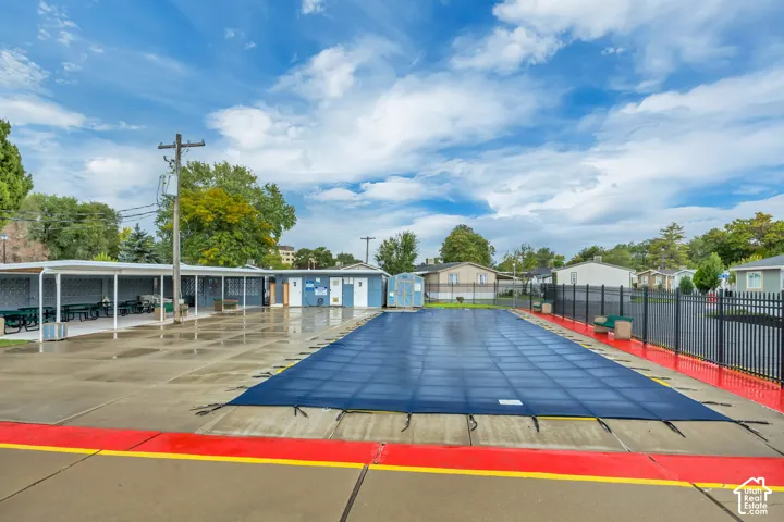 Outdoor pool with a dark blue cover, surrounded by concrete decking and a black metal fence