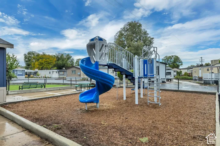 Play structure with a spiral slide, open-rung ladder, and multiple platforms, set on a wood chip ground cover