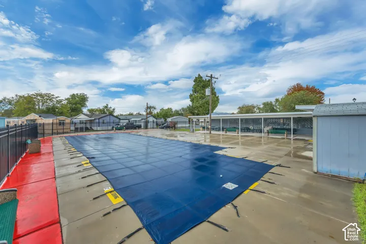 Outdoor pool with a safety cover, concrete decking, and a black metal fence
