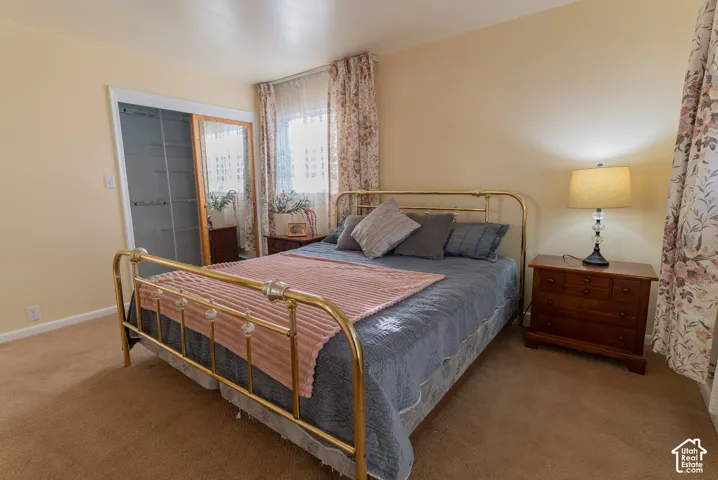 Bedroom featuring neutral wall paint, carpet flooring, a window with sheer and floral curtains, and a built-in closet with sliding mirrored doors