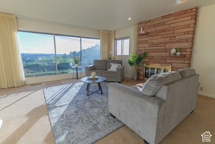Expansive windows, stone-clad fireplace, built-in shelving, brass firebox, and neutral carpeting