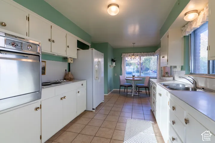 White cabinetry with brass-tone hardware, built-in oven, tile flooring, and a large window with natural light