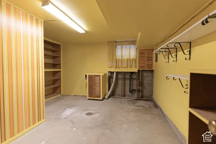 Concrete flooring, built-in shelving, mounted wall shelves with decorative brackets, window with curtains, and built-in cabinetry