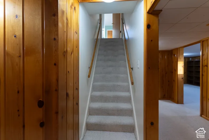 Carpeted staircase with a wood handrail, paneled wood walls, and a recessed ceiling light
