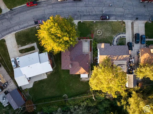 Aerial view showcasing a residential property featuring mature landscaping with vibrant yellow-leafed trees, manicured lawn, brick exterior with pitched roofline, paved driveway, and detached garage structure