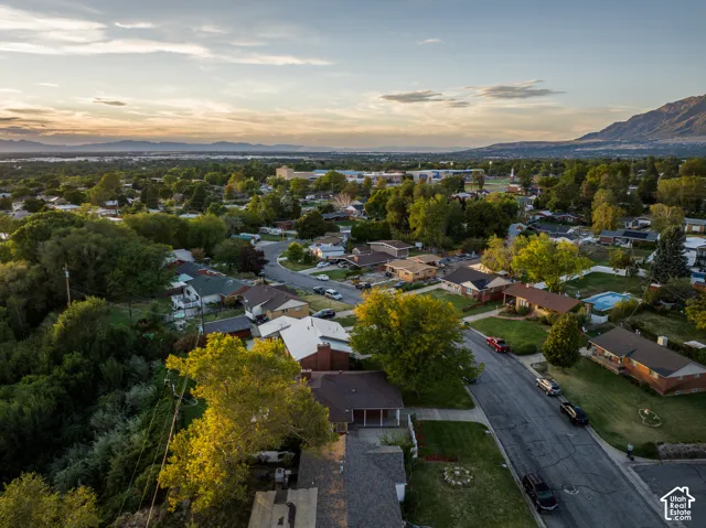 Residential neighborhood with a curved street layout, mature trees, mountain backdrop, and distant water body