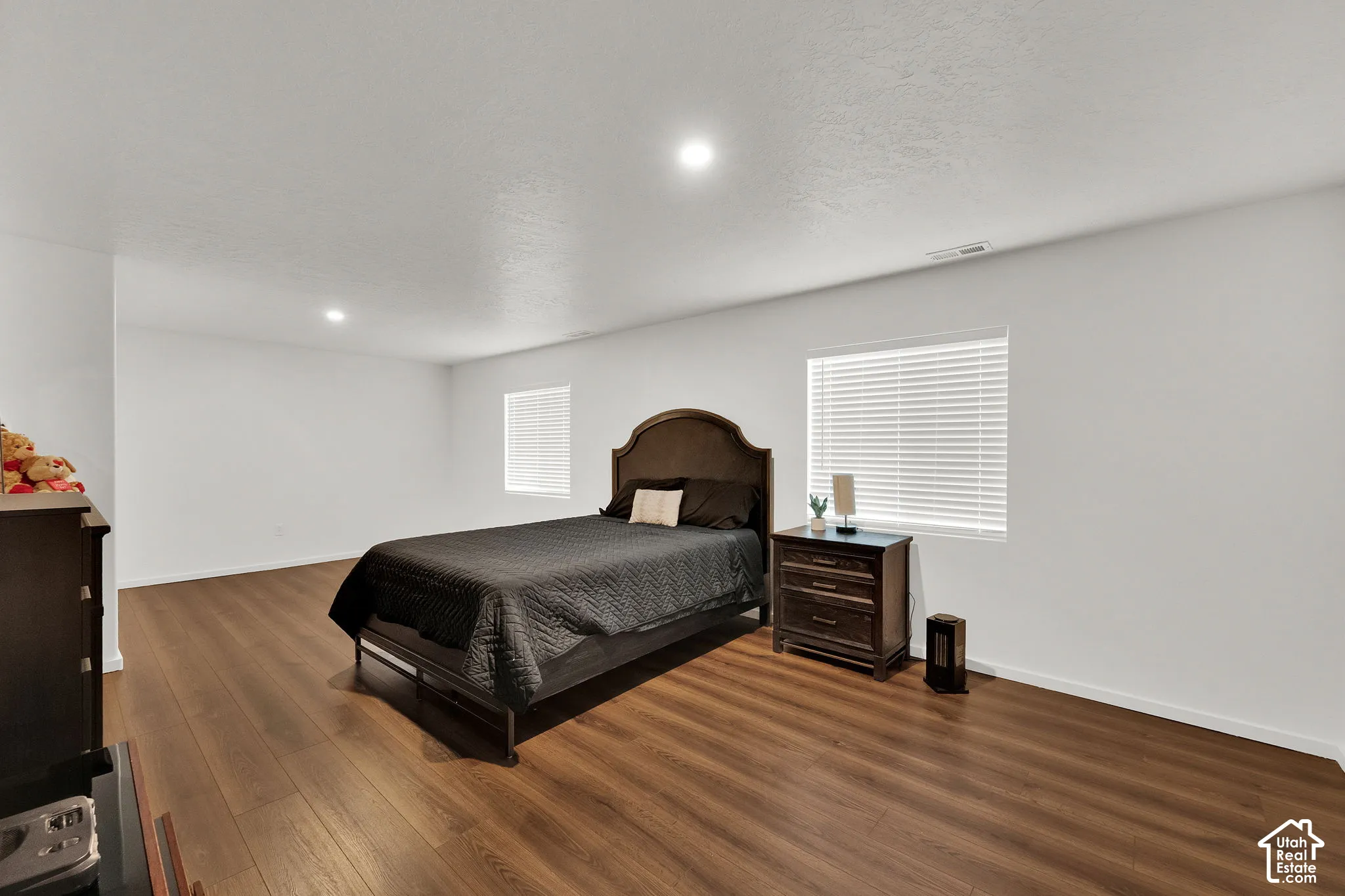 Expansive room with wood-finish flooring, recessed lighting, and two windows with blinds