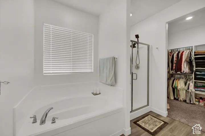 Soaking tub with chrome fixtures, glass-enclosed shower, wood-finish flooring, and a walk-in closet