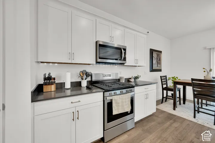 White shaker-style cabinetry, dark countertops, stainless steel appliances, and wood-finish flooring