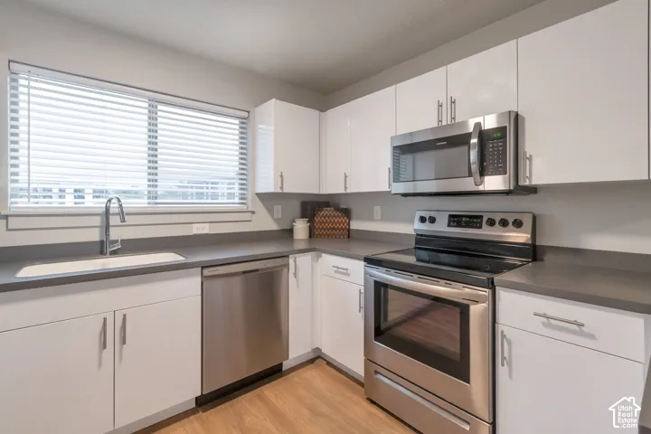White cabinetry, stainless steel appliances, wood-finish flooring, and a window above the sink
