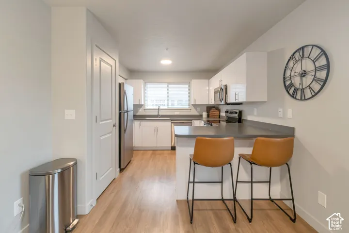 Kitchen featuring white flat-panel cabinetry, a stainless steel refrigerator, dark countertops, a breakfast bar, and wood-finish flooring