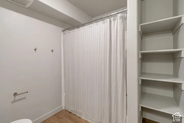 Built-in shelving, wood-finish flooring, and a shower with a chrome rod