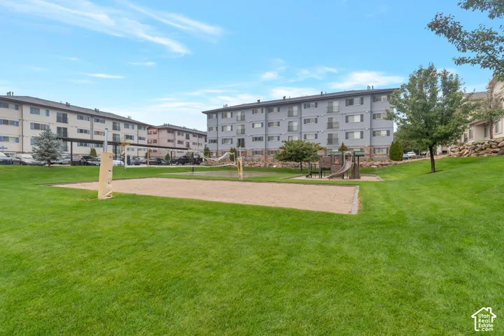 Manicured green space with a sand volleyball court, integrated play structure, and mature trees