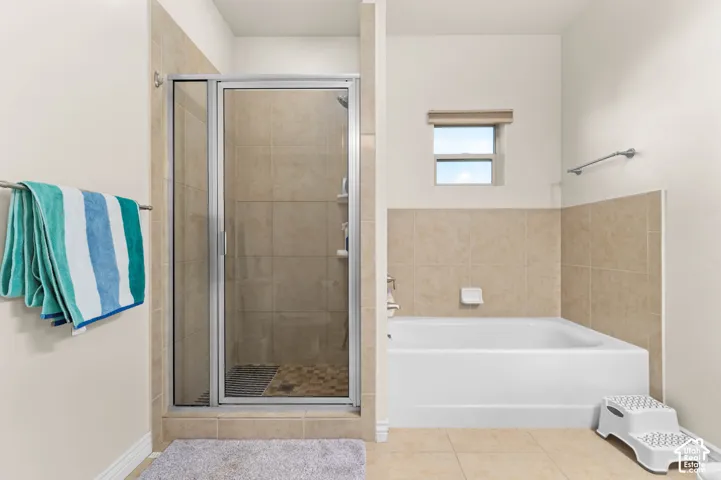 Enclosed shower with clear glass door, full-size bathtub, tiled shower surround, tiled flooring, and a privacy window