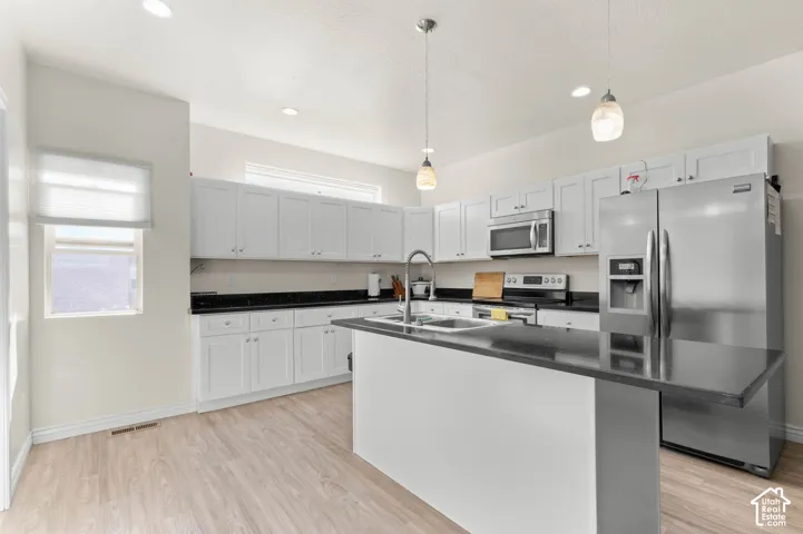 Kitchen featuring white cabinetry, dark countertops, stainless steel appliances, a center island, and wood-finish flooring