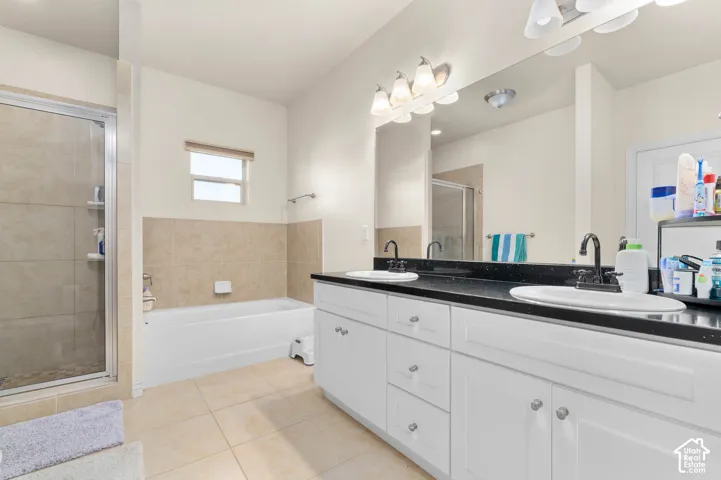 Dual basin vanity with white cabinetry and dark countertops, separate shower enclosure with tile surround, and a built-in bathtub with tiled wainscoting