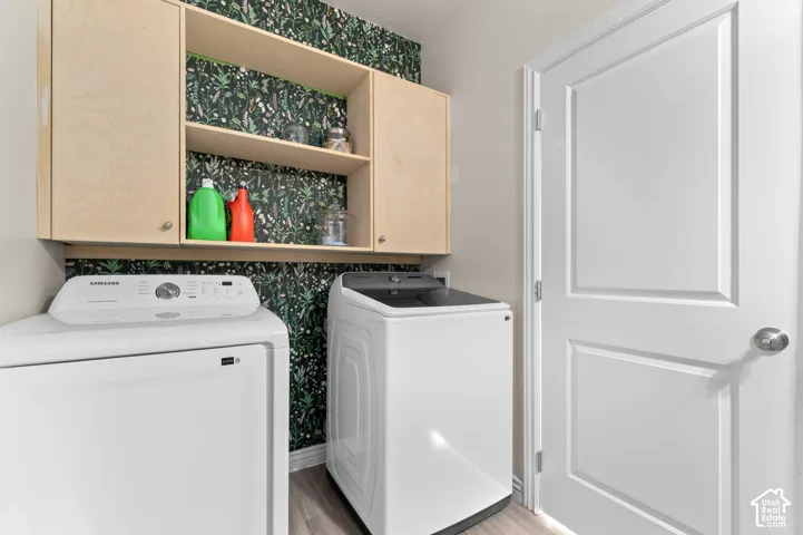 Light wood-finish cabinetry with open shelving, contrasting patterned wall covering, white paneled interior door, and wood-finish flooring