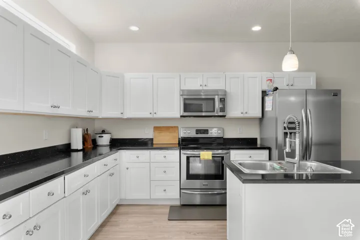 White shaker-style cabinetry with chrome hardware, black speckled countertops, stainless steel appliances, and a kitchen island with an undermount sink