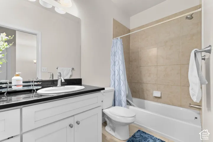 Vanity with white cabinetry and dark countertop, integrated sink, large wall-mounted mirror, and a full bathtub with tiled surround