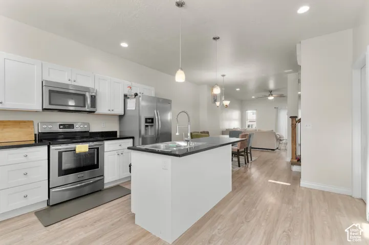 Kitchen featuring stainless steel appliances, white cabinetry, dark countertops, and a central island with an integrated sink