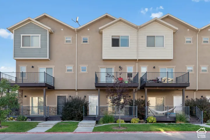 Multi-level townhome featuring a stucco exterior, multiple balconies with dark railings, and a ground-level patio