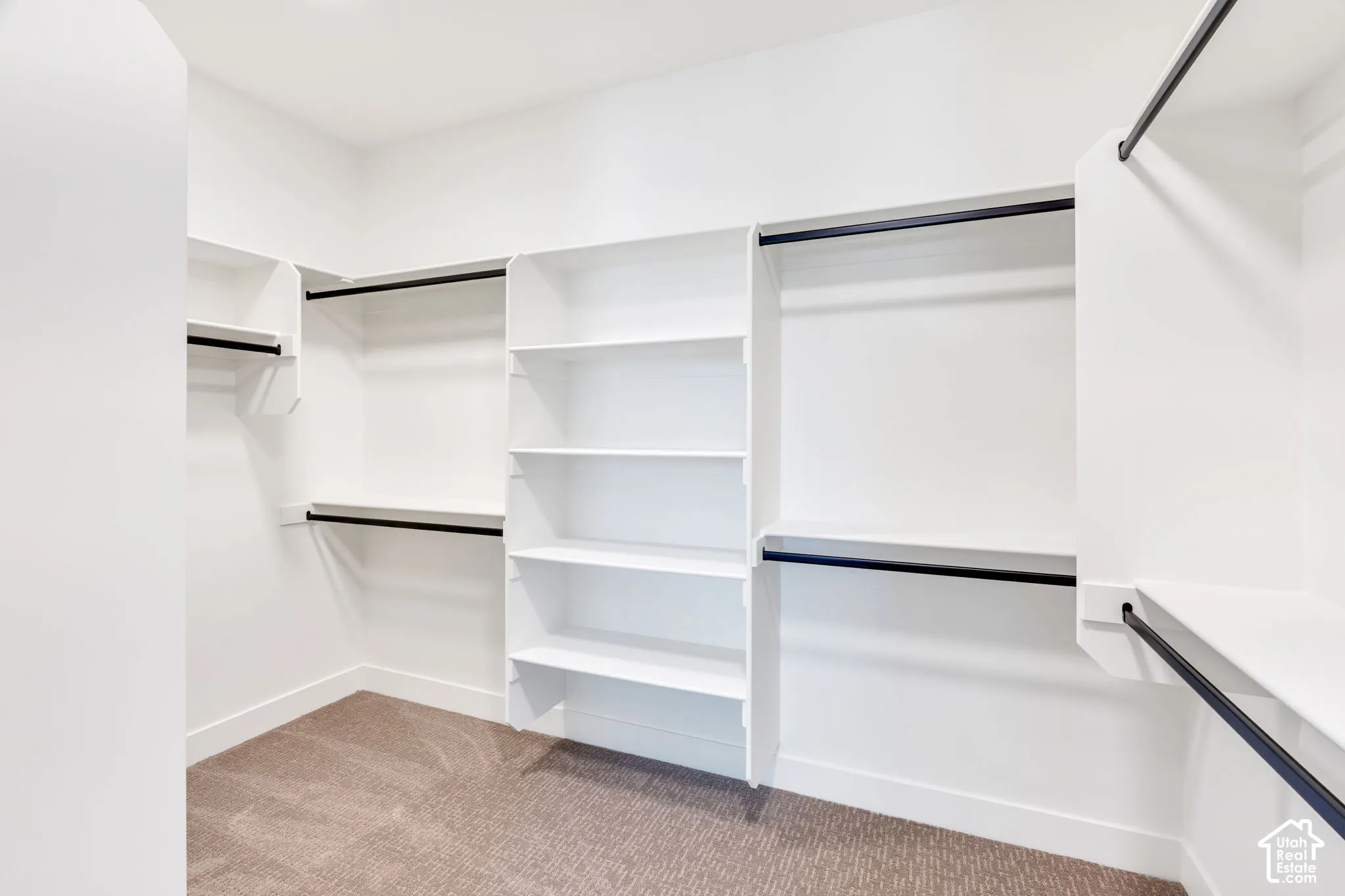 Walk-in closet with integrated shelving, multiple hanging rods, and neutral-toned carpeting