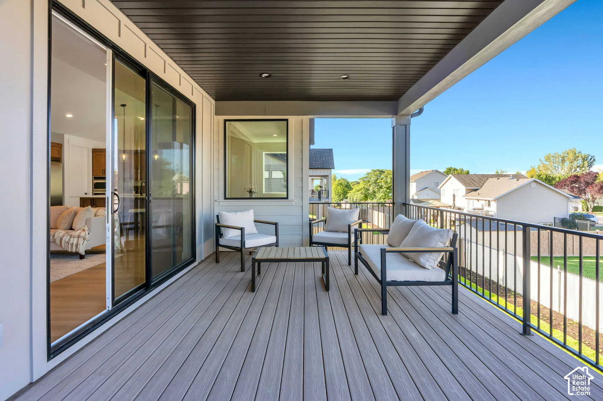Covered outdoor patio featuring composite decking, black metal railings, and a large sliding glass door