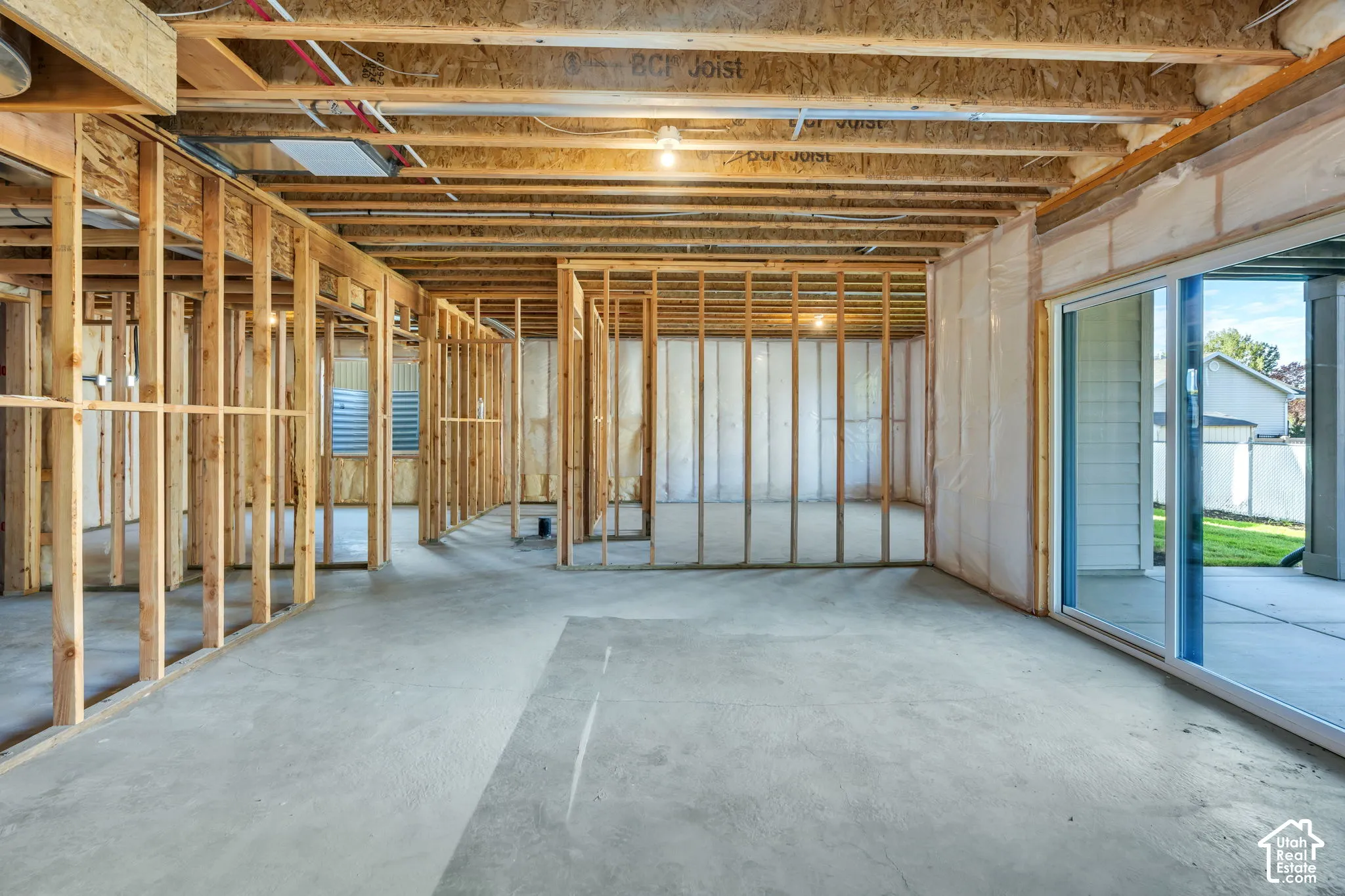 Unfinished basement featuring exposed wood framing, concrete flooring, sliding glass patio door, and exposed ceiling joists