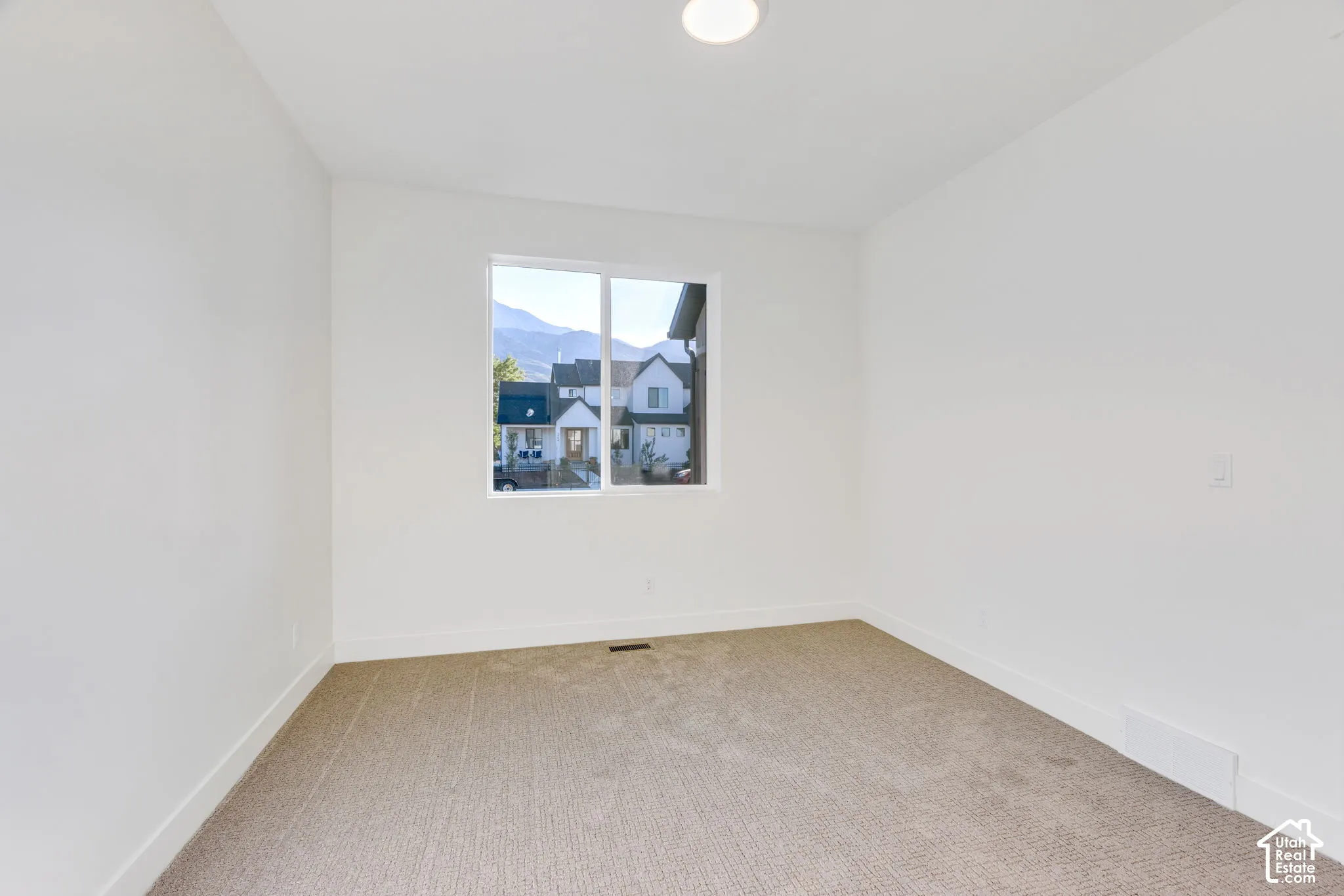 Bright interior with neutral carpeting, white walls, a recessed ceiling light, and a window framing a mountain backdrop