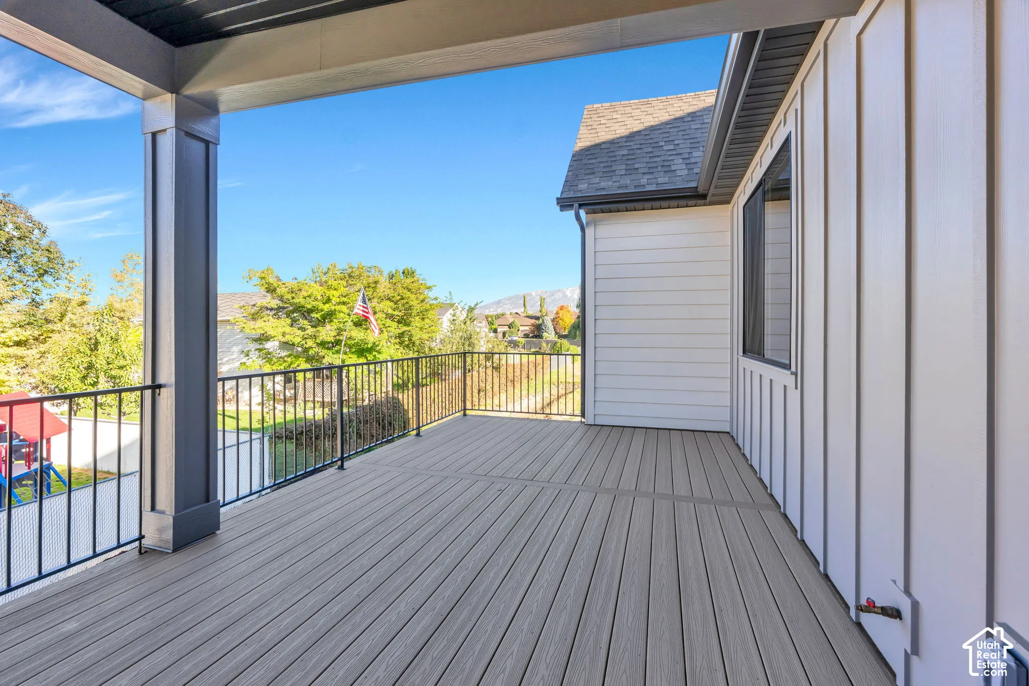 Expansive outdoor deck featuring wood-finish flooring, black metal railings, and a solid overhead covering