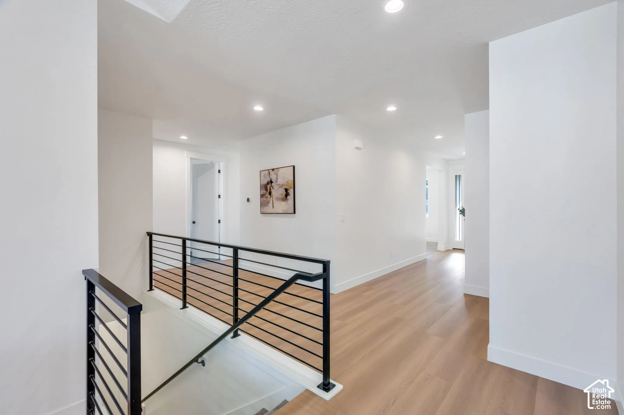 Modern black metal horizontal bar railing with wood-finish flooring, recessed lighting, and crisp white walls