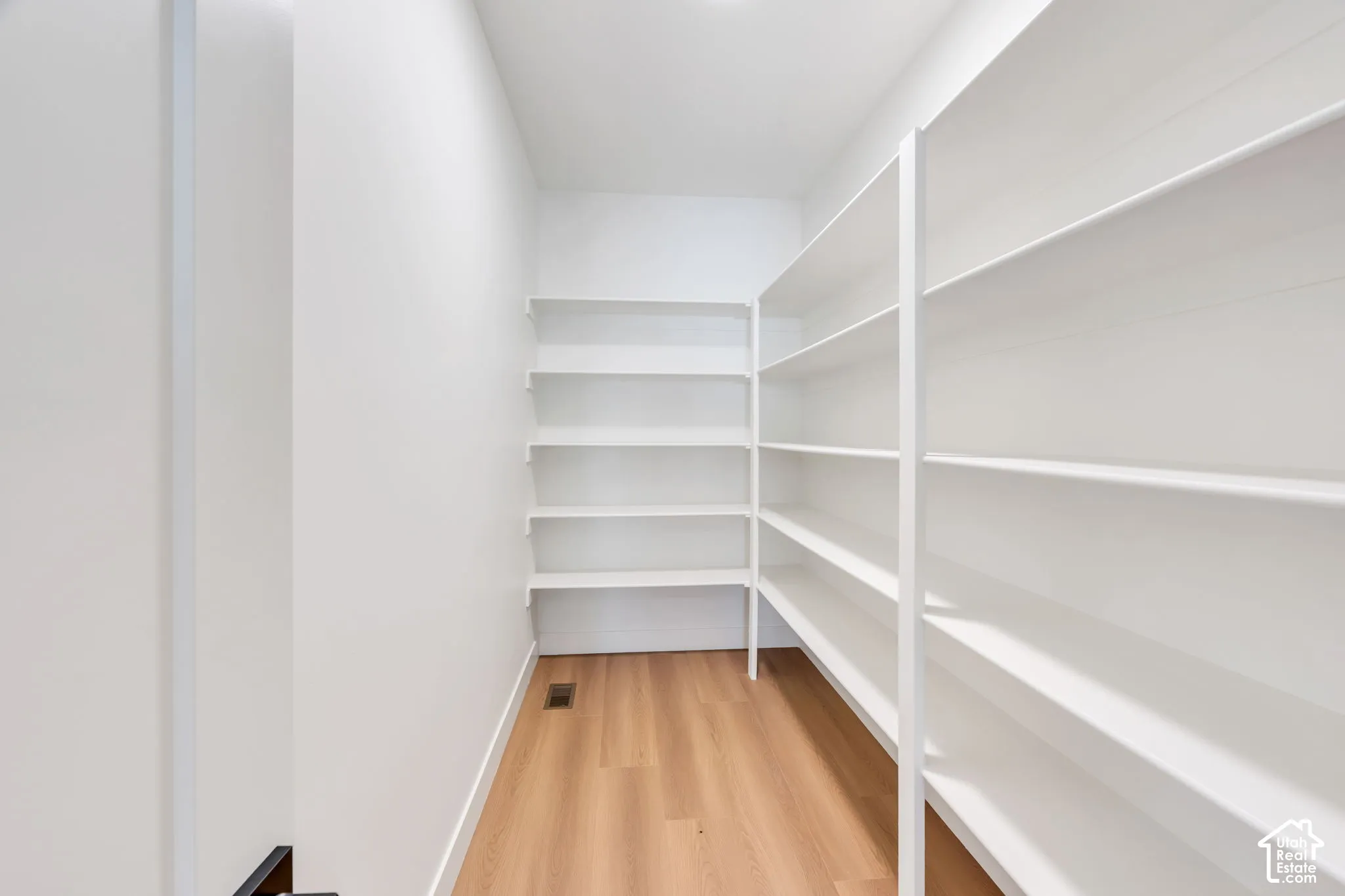 Walk-in pantry with extensive built-in white shelving and wood-finish flooring