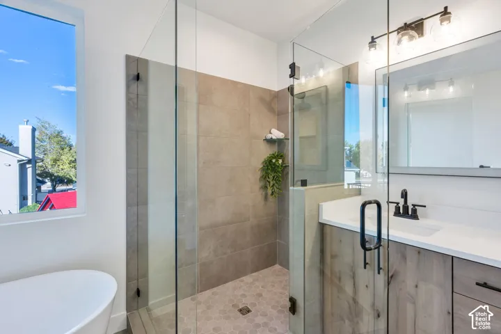 Spacious bathroom featuring a freestanding tub, glass-enclosed shower with tile surround, wood-finish vanity with countertop, and modern lighting fixture