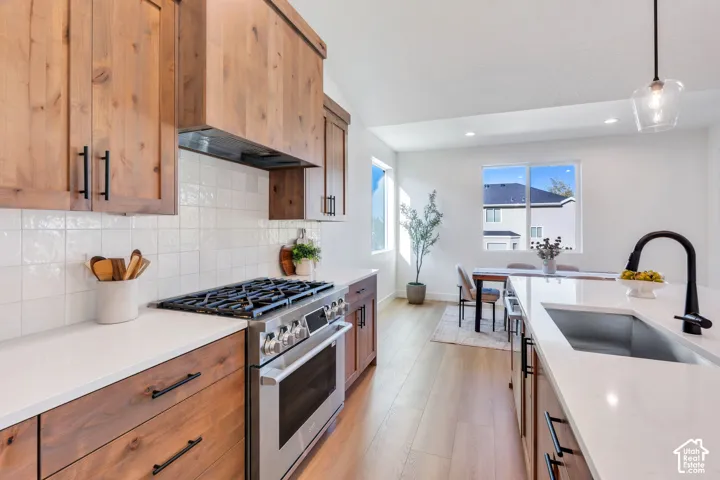 Kitchen featuring wood cabinetry, white tile backsplash, stainless steel range, and a kitchen island with an undermount sink and black faucet