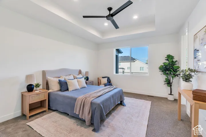 Tray ceiling with recessed lighting, ceiling fan, large window, and light-toned carpeting
