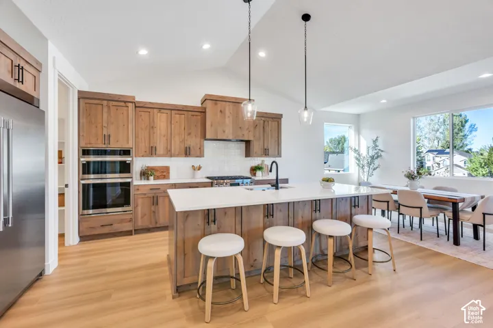 Kitchen featuring natural wood-finish cabinetry, stainless steel double ovens, a large center island with counter seating, and an adjacent dining area with expansive windows