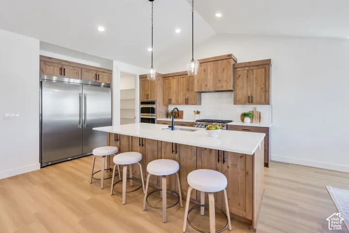 Contemporary kitchen featuring custom wood cabinetry, white quartz countertops, stainless steel appliances including a built-in refrigerator and dual wall ovens, a gas cooktop with hood, and a large waterfall-edge island with seating for four