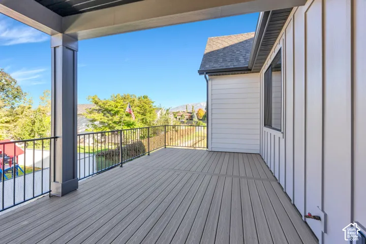 Expansive outdoor deck featuring wood-finish flooring, black metal railings, and a solid overhead covering