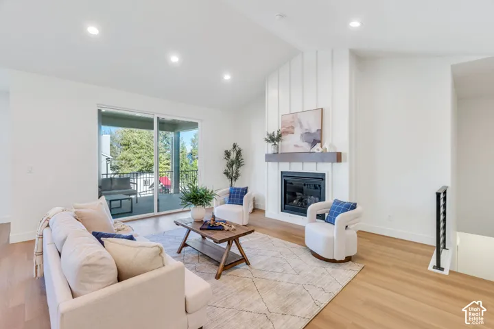 Vaulted ceiling, recessed lighting, wood-finish flooring, fireplace with shiplap-style surround and wood mantle, and sliding glass door to exterior