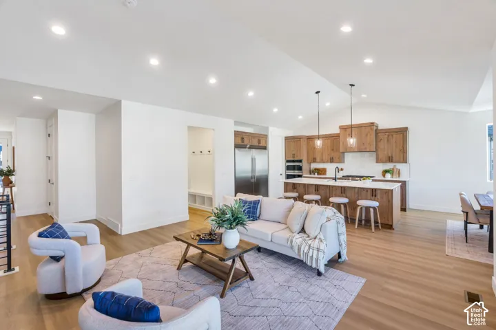 Vaulted ceilings with recessed lighting, wood-finish flooring, and a kitchen featuring wood cabinetry, stainless steel appliances, and a central island with pendant lighting