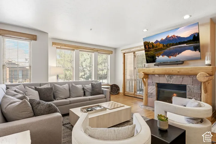 Stone fireplace with a log mantel, recessed lighting, wood-finish flooring, and multiple windows with blinds