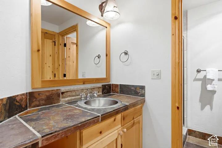 Vanity with a stainless steel sink, natural wood cabinetry, multi-colored stone countertop, and a coordinating wood-framed mirror