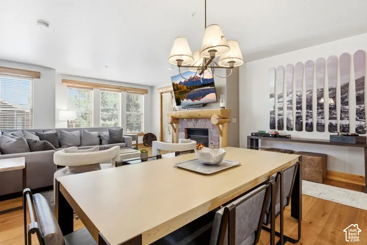 Open-concept living space featuring wood-finish flooring, a stone-surround fireplace with a log mantel, and a multi-light chandelier